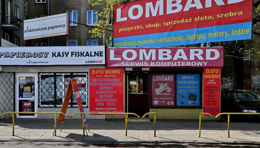Banery lombardów i sklepów z elektroniką na tle budynku mieszkalnego.